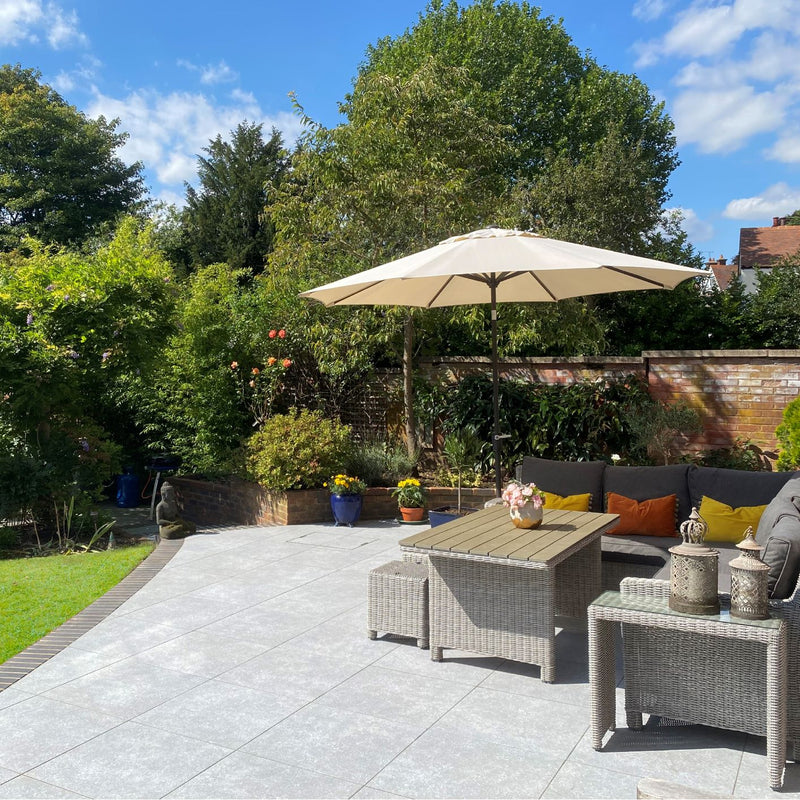 Lifestyle image showing House of Mosaics Bombay grey outdoor porcelain tile being used to create an outdoor living space in the garden, with a set of grey table and chairs