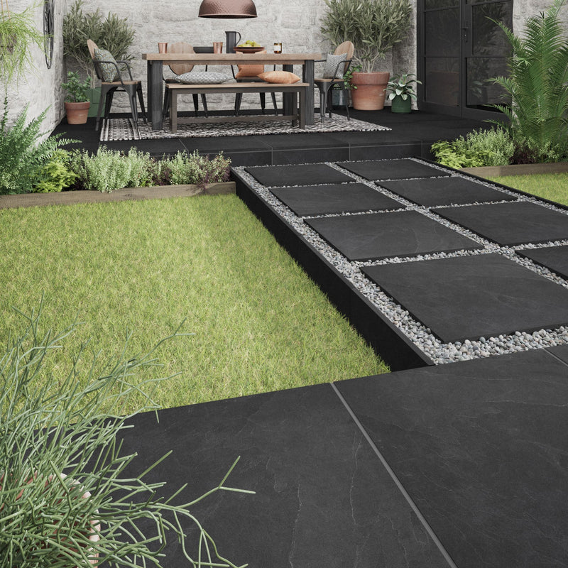 Lifestyle image of the House of Mosaics outdoor porcelain Black Slate tile, showing the tiles being used as stepping stones leading to a raised area for a perfect outdoor living space